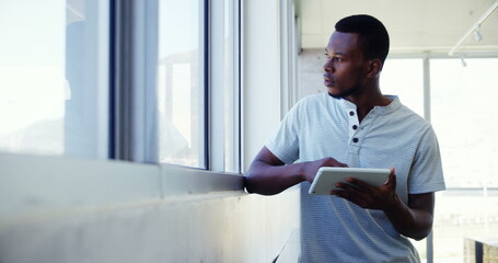 Executive standing near window and using digital tablet in office