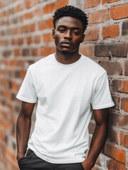 Obraz premium Young Black man with short curly hair wearing a white t-shirt, standing confidently against a brick wall background with a serious expression