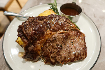 close up of roasted beef steak with barbecue sauce on the side and herbs on a white plate with copyspace