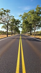 Naklejka premium Wide shot of an asphalt road with two yellow lines stretching into the distance as trees line the edge of the road, trees, traffic lanes
