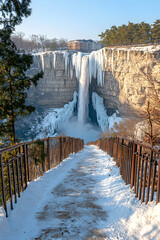 Frozen waterfall winter landscape, snow pathway leads to viewing point.
