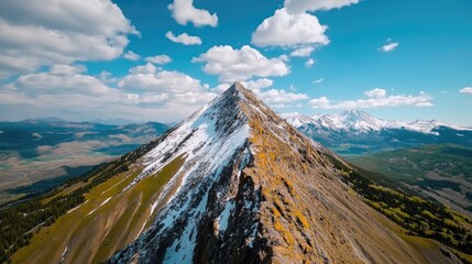 Fototapeta premium Stunning Aerial View of Snow-Capped Mountain Peak Under a Vibrant Blue Sky with Fluffy Clouds in a Picturesque Landscape
