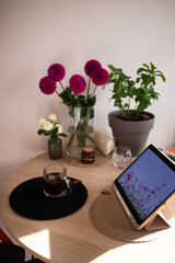 Served kitchen wooden table with pink dahlias in a glass vase. iPad, candles, cup of coffee.