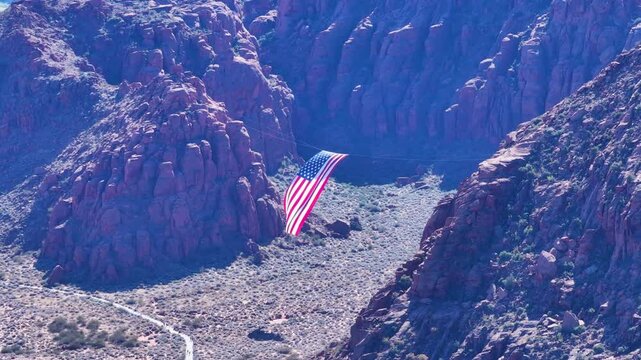 Aerial USA flag between mountains Utah pull. American USA flag between two red rock mountains. Celebration of Veterans Day in Southwestern desert. Snow Canyon Park. Patriotic display of huge fla