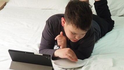 Smiling teenage school kid using tablet computer, relaxing on sofa at home, watching learning video, movie, online class, listening to music, communicates with friends, social networks