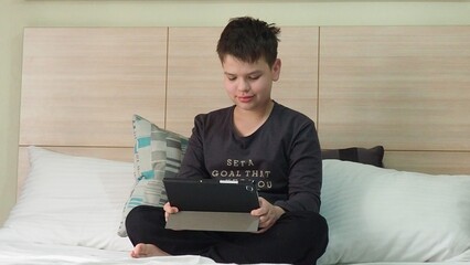 Smiling teenage school kid using tablet computer, relaxing on sofa at home, watching learning video, movie, online class, listening to music, communicates with friends, social networks