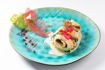 Chicken Rolls with White Sauce and Edible Flower on a Plate Against a White Background