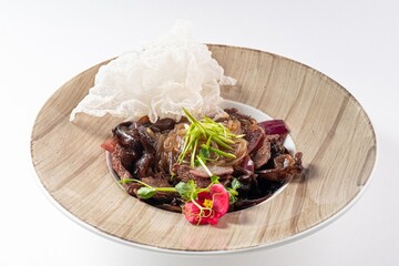 Asian Salad with Beef, Greens, Herbs, and Edible Flower on a Plate Against a White Background