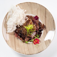Asian Salad with Beef, Greens, Herbs, and Edible Flower on a Plate Against a White Background