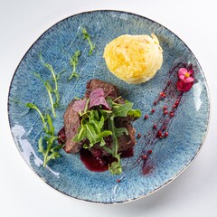 Beef Medallions with Arugula, Mashed Potatoes, and Sauce on a Plate Against a White Background