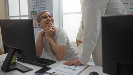 Woman smiling at colleague in modern office while discussing work, with documents and computers...