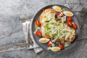 Breaded schnitzel Caesar salad with crispy chicken meat, eggs, parmesan, iceberg lettuce and tomatoes close-up in a plate on the table. horizontal top view from above