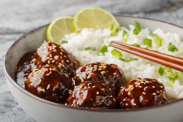 Asian meatballs coated in the sweet and spicy sauce made with sriracha, soy sauce, ginger, honey and garlic served with rice closeup on the bowl on the table. Horizontal