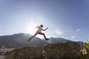 A man is jumping over a rock in the mountains