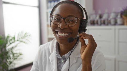 Woman smiling in pharmacy store wearing headset and white coat, engaging in customer service.