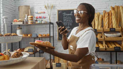Woman happily taking photo with mobile phone in bakery shop holding a plate with pastries...