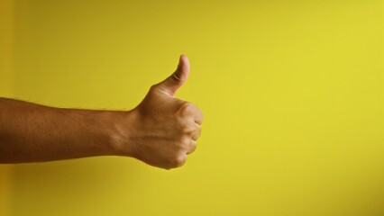 Man giving thumbs up gesture against vibrant yellow background with focus on hand and fingers...