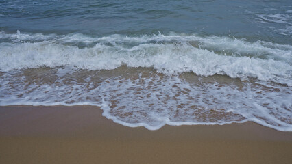 A peaceful outdoor scene of gentle waves washing onto a sandy beach, capturing the soothing motion of the ocean and foam against the shore.