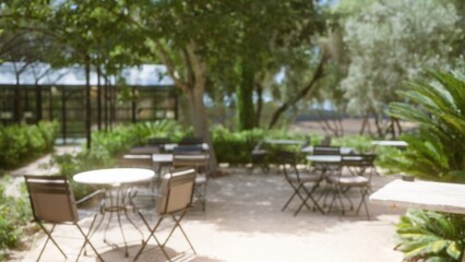 Obraz premium Blurred outdoor cafe setting in mallorca with defocused tables, chairs, and lush greenery in the background under bright sunlight.