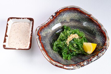 Chuka Seaweed Salad with Nut Sauce and Lemon on a Plate Against a White Background