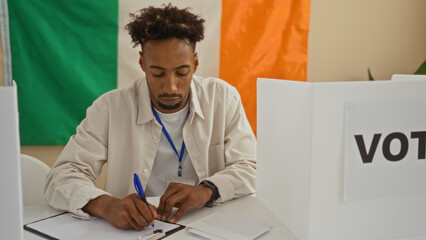 Young african american man taking notes inside an electoral college room with an irish flag in the background.