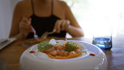 Young woman dining indoors at a fancy restaurant with beautifully plated gourmet food in front of...