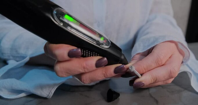 Detailed view of a jeweler using a handheld diamond tester to check the authenticity of a gemstone on a ring