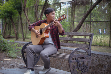 Portrait of Asian man playing guitar in outdoor park