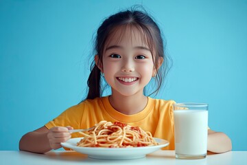 A cute Asian girl wearing a yellow t-shirt, eating pasta with tomato sauce and drinking milk, sitting at a white table against a light blue background.