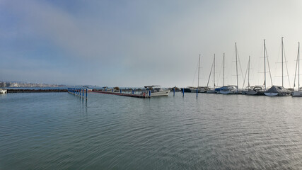 Peaceful marina with docked sailboats on a calm misty morning, emphasizing tranquility and leisure, perfect for summer getaways