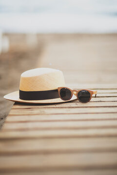 Close-up of a Straw hat and sunglasses on a wooden walkway on the beach