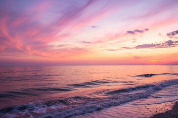 Fototapeta premium Serene ocean waves gently caress the shore under a breathtaking sunset sky, painting the horizon with vibrant hues of pink and orange.