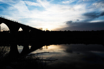 Silhouette of an Arched Bridge at Sunset Reflecting on Calm Waters in Fuentes Claras, Avila, CyL