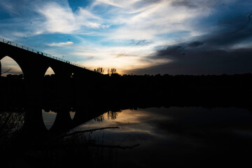 Silhouette of an Arched Bridge at Sunset Reflecting on Calm Waters in Fuentes Claras, Avila, CyL