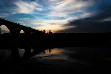 Silhouette of an Arched Bridge at Sunset Reflecting on Calm Waters in Fuentes Claras, Avila, CyL