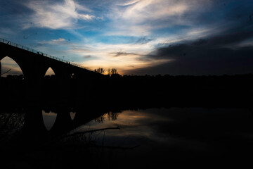 Silhouette of an Arched Bridge at Sunset Reflecting on Calm Waters in Fuentes Claras, Avila, CyL