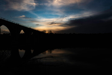 Silhouette of an Arched Bridge at Sunset Reflecting on Calm Waters in Fuentes Claras, Avila, CyL
