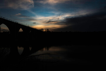 Silhouette of an Arched Bridge at Sunset Reflecting on Calm Waters in Fuentes Claras, Avila, CyL