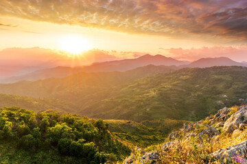 highland mountain landscape of beautiful sunset or sunrise with nice mountain peaks and slopes, green and golden hills and majestic cloudy sky on background