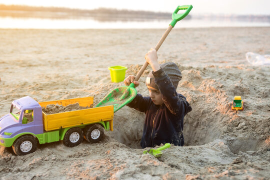 A child playing on the beach with a toy truck and shovel, digging a hole in the sand. The scene captures the joy and creativity of outdoor playtime by the water.