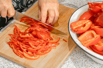 Cook uses a knife to shred a red bell pepper on a wooden board. Close-up