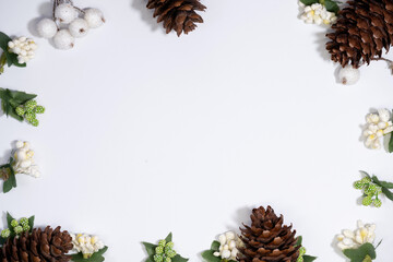 A festive frame made of pinecones, cinnamon sticks, star anise, and holly leaves on a white...