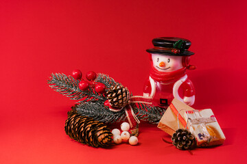 Festive arrangement with a snowman figurine, pinecones, and gifts on a red background.