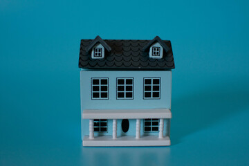 A small model house with a gray roof, placed next to a key and stacks of coins on a blue...