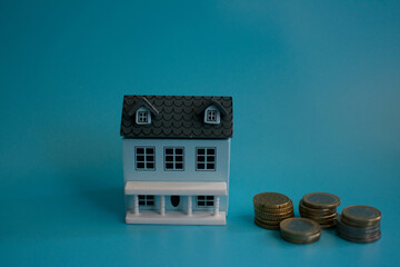 A small model house with a gray roof, placed next to a key and stacks of coins on a blue...