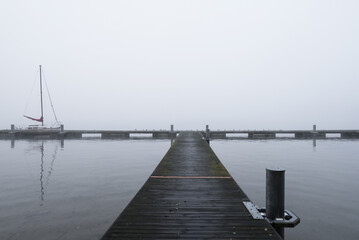 Obraz premium LANDSCAPE BY THE LAKE - A sailboat at the pier on a misty morning