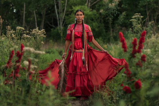 Native American woman wearing a red dress, standing gracefully in a lush green field