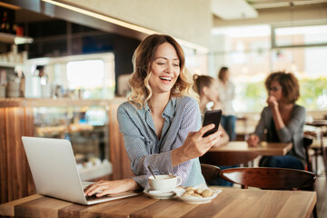 Fototapeta premium Young woman using a phone while having coffee in a cafe