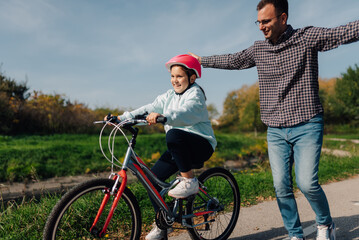 Father teaches daughter how to ride bicycle in park