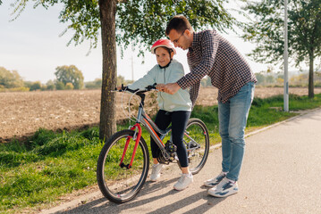 Obraz premium Father teaching daughter riding bicycle outdoors in a park